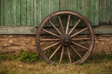 Fototapeta premium Antique wooden wagon wheel mounted on a weathered wall with grass and rustic texture