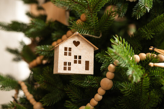 A charming wooden miniature house ornament hangs on a Christmas tree - Powered by Adobe