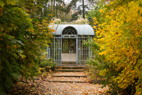 A secluded metal gazebo at the end of a winding path, surrounded by vibrant autumn foliage.
