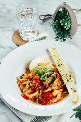 A delectable seafood pasta dish with a glass of water, garnished with fresh herbs and a slice of garlic bread