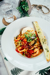 A plate of seafood pasta with a glass of water, fresh and appetizing, set on a marble table