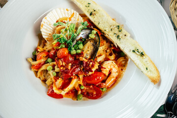 Delicious seafood pasta dish with a side of toasted garlic bread, artfully presented on a round, white plate