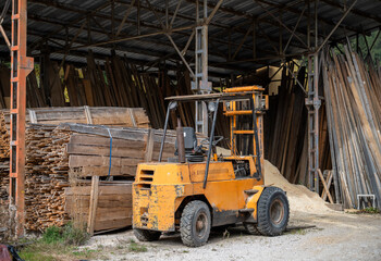 Old yellow forklift inside carpentry workshop with wooden planks and construction materials