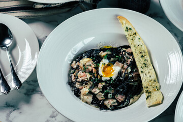 Delicious pasta dish with egg yolk and garlic bread, a culinary delight. The meal is served on a white plate with silverware, set on a marble table