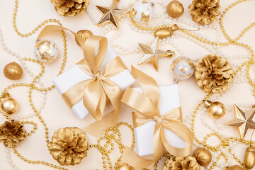 Two elegant gift boxes with golden ribbons surrounded by Christmas and New Year decorations. Flat lay with pine cones, stars, and pearls in soft golden tones