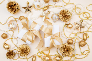 Two elegant gift boxes with golden ribbons surrounded by Christmas and New Year decorations. Flat lay with pine cones, stars, and pearls in soft golden tones