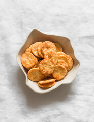 Cheddar cheese cracker in a ceramic bowl on a light background, top view