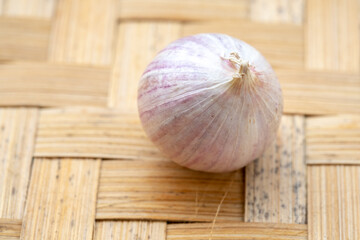A single whole bulb of solo garlic, showing its purple-striped papery skin, rests on a traditional woven bamboo tray.