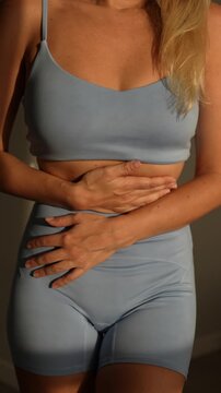Close-up of a young woman holding her stomach in discomfort. Possible stomach pain, digestion issues, or menstrual cramps. Expressing body awareness and sensitivity