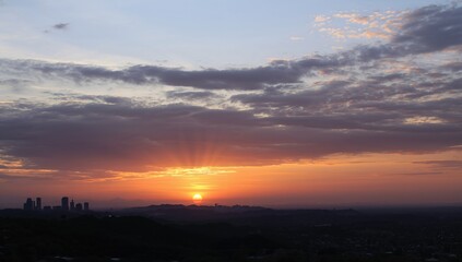 Obraz premium A stunning fusion of urban and natural elements as the sun sets behind gentle hills, painting the sky with hues of amber and lavender.