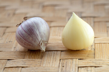 A single peeled solo garlic clove and a whole garlic bulb sitting side-by-side on a traditional woven bamboo tray.