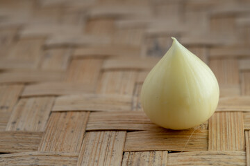 A single peeled solo garlic clove with a smooth, pale-yellow surface, sitting on a traditional woven bamboo mat.