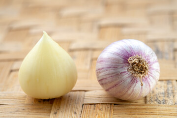 A single peeled solo garlic clove and a whole garlic bulb sitting side-by-side on a traditional woven bamboo tray.