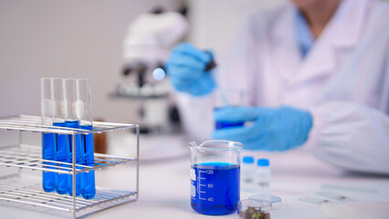 Fototapeta premium Asian adult scientist conducts chemical experiment in laboratory pipetting blue liquid into beaker with test tubes for research and discovery