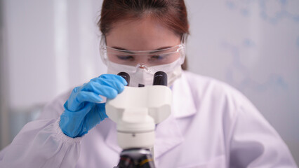 Asian woman scientist researcher conducting scientific analysis using microscope in modern laboratory for medical and biological innovation