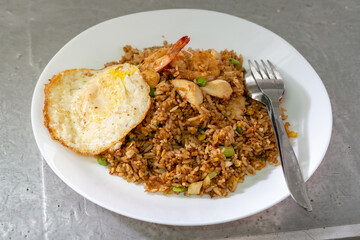 A plate of Indonesian nasi goreng, or fried rice, is served with shrimp, meatballs, a sunny-side-up fried egg, and slices of fresh cucumber.