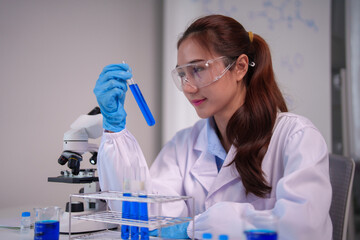 Asian female scientist conducts chemical experiment examines blue liquid test tube professional laboratory setting performing medical biological research