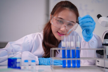 Asian woman scientist conducts chemical experiment modern laboratory using dropper analyzing blue liquid in test tubes precise research work
