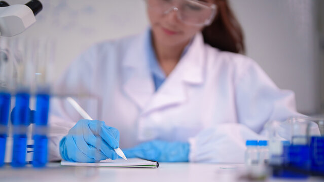 Asian adult female scientist conducting research laboratory experiment recording observations data analysis innovation healthcare science lab biotechnology drug development