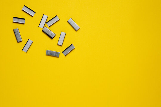 A top-down view of several strips of metal staples scattered in the top-left corner of a bright yellow textured background.