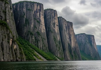 Dramatic cliffs rise from the calm water of a norwegian fjord under a cloudy sky