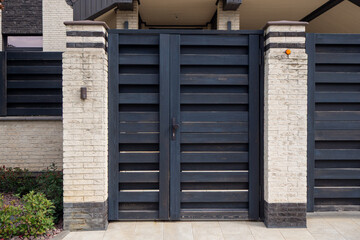 Black horizontal slat gate between stone pillars. Modern entrance for private residence or luxury property with clean architectural lines. Real photo