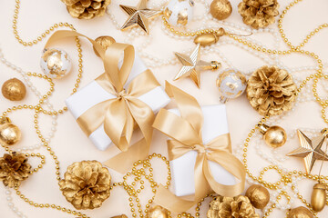 Two elegant gift boxes with golden ribbons surrounded by Christmas and New Year decorations. Flat lay with pine cones, stars, and pearls in soft golden tones