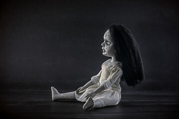 Scary cracked doll with black hair on dark background