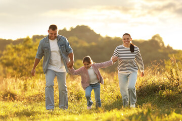 Happy family holding hands and running in field at sunset