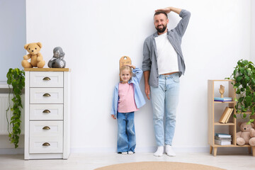 Father and daughter measuring their heights near white wall at home