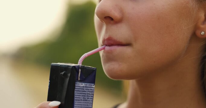 Young woman enjoying a drink with a straw on a sunny day outdoors in a natural setting