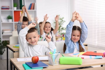 Cute children raising hands at wooden desks during art lesson in elementary school