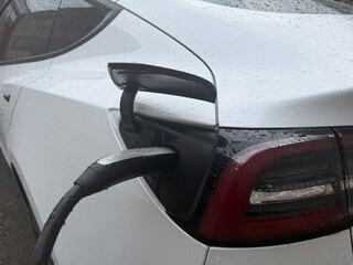 Electric car charging in the rain. Close-up of a white electric vehicle plugged into a charging station, with water droplets on the car surface. Concept of clean energy, eco-friendly transportation.