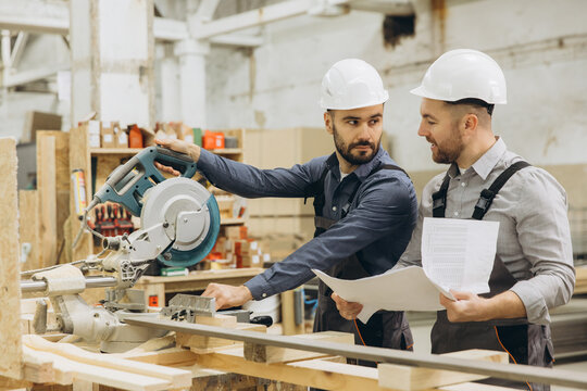 Two carpenters discussing woodworking project using circular saw in workshop - Powered by Adobe