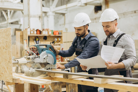 Carpenters working with circular saw and blueprint in workshop