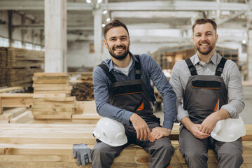 Two carpenters smiling and sitting on wood planks in workshop