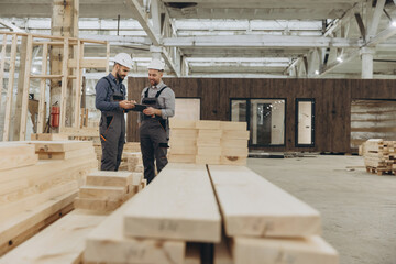 Fototapeta premium Construction workers using tablet and inspecting wooden planks in factory