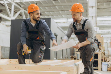 Construction workers building wooden frame using blueprint in factory