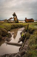 Decaying wooden shipwreck and rusting metal hull on marshes under overcast sky