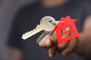 Close up of a hand holding a key with house-shaped keychain representing home ownership, real estate, mortgage, and investment.