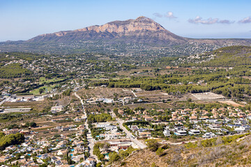 An aerial view of the Javea neighborhood with modern villas nestled among forests against the backdrop of Mount El Montgo.