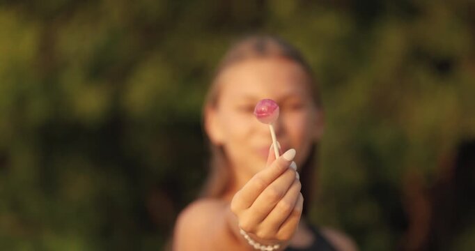 Young girl enjoys lollipop while smiling in a sunny park during late afternoon