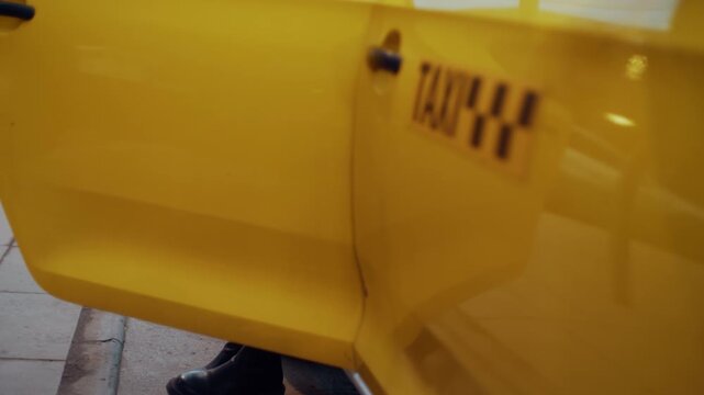 Stylish girl wearing high boots opening the door of a yellow taxi and getting inside the car