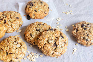 A freshly baked oatmeal raisin cookie with visible oats placed on natural linen tablecloth background.
