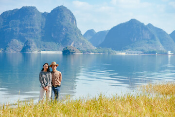 Obraz premium Chinese couple enjoying Quyang Lake (Quyanghu) karst peaks landscape standing on grassland along lakeside in winter in Jingxi county, Baise city, Guangxi province, China