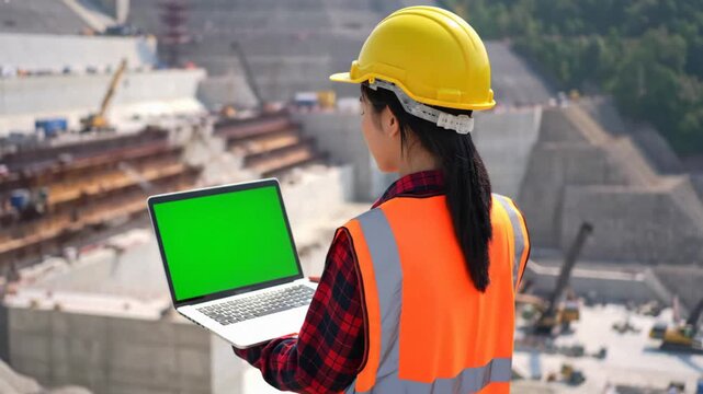Asian Female Project Manager Engineer Holding Laptop with Green Screen Chroma Key, Supervising Massive Dam Infrastructure Construction Project, Mock-up for Industrial Presentation