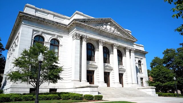 A stately, white classical building with columns, under a blue sky, and trees