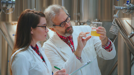 Brewers in lab coats inspect a beaker of beer in a modern craft brewery, conducting quality control tests and monitoring production standards, fermentation and analysis techniques