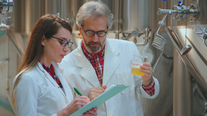 Brewing professionals in lab coats performing quality control on a beer sample, examining the liquid in a beaker while taking notes, ensuring high standards in a modern brewery setting