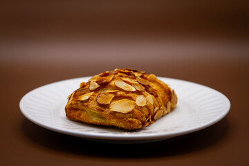 Almond Croissant on White Plate with Brown Background – Freshly Baked Pastry with Sliced Almond Topping